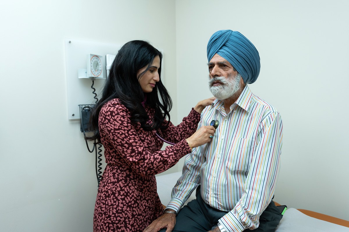 Doctor examining an older man with a stethoscope in a bright clinic exam room
