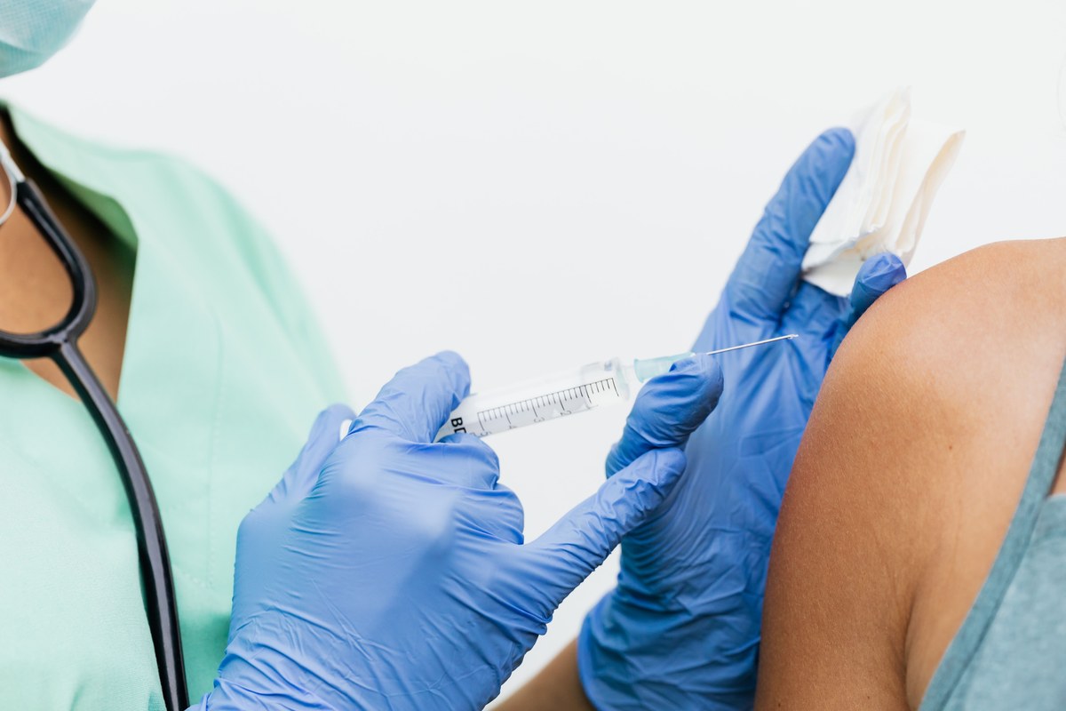 Close-up of a clinician in gloves giving an intramuscular vaccine injection into a patient's upper arm