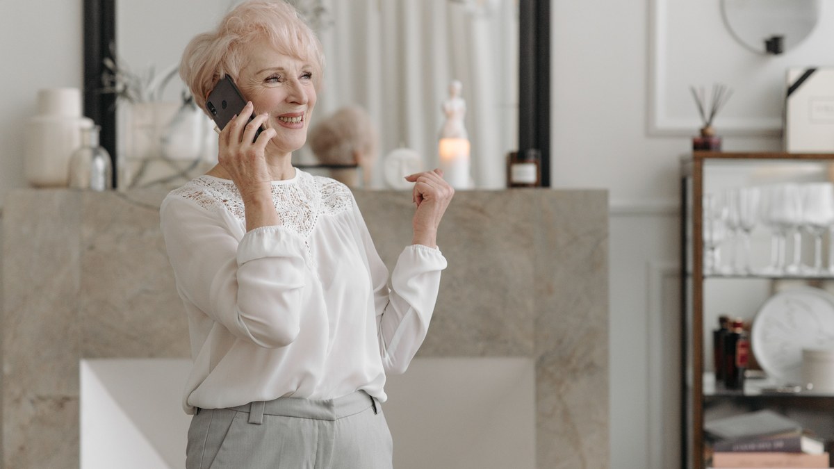 Older woman in a white blouse smiling during a phone call in a bright living room