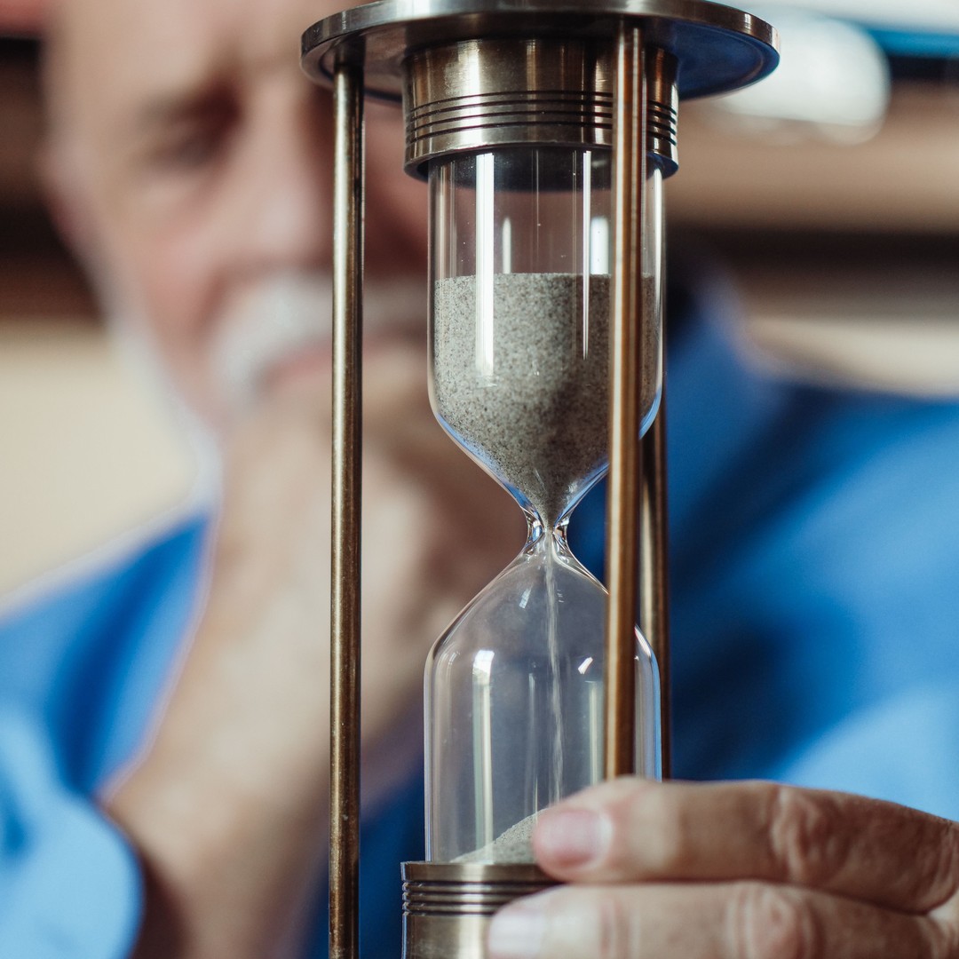 An older man holding up an hourglass and watching the sand run down