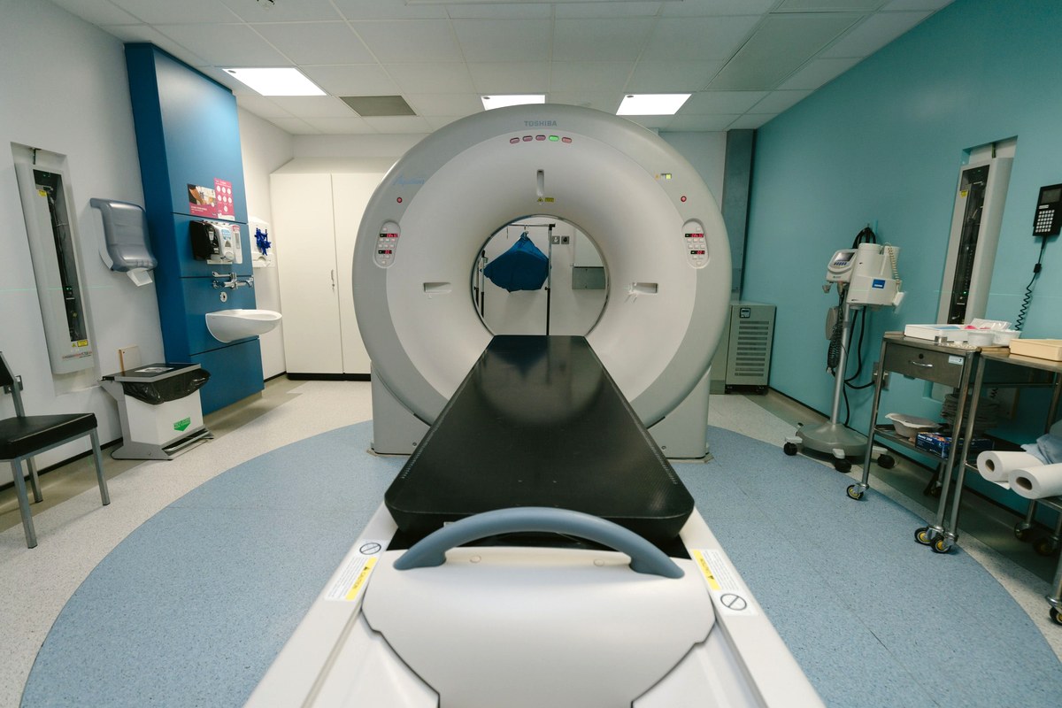 A CT scanner seen head-on in a quiet hospital imaging room, its patient table extended and empty
