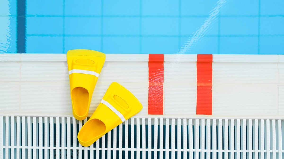Yellow swim fins resting on the white tiled edge of a bright blue swimming pool