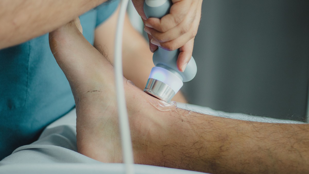 A physical therapist holding a therapeutic ultrasound head with gel against a patient's lower leg