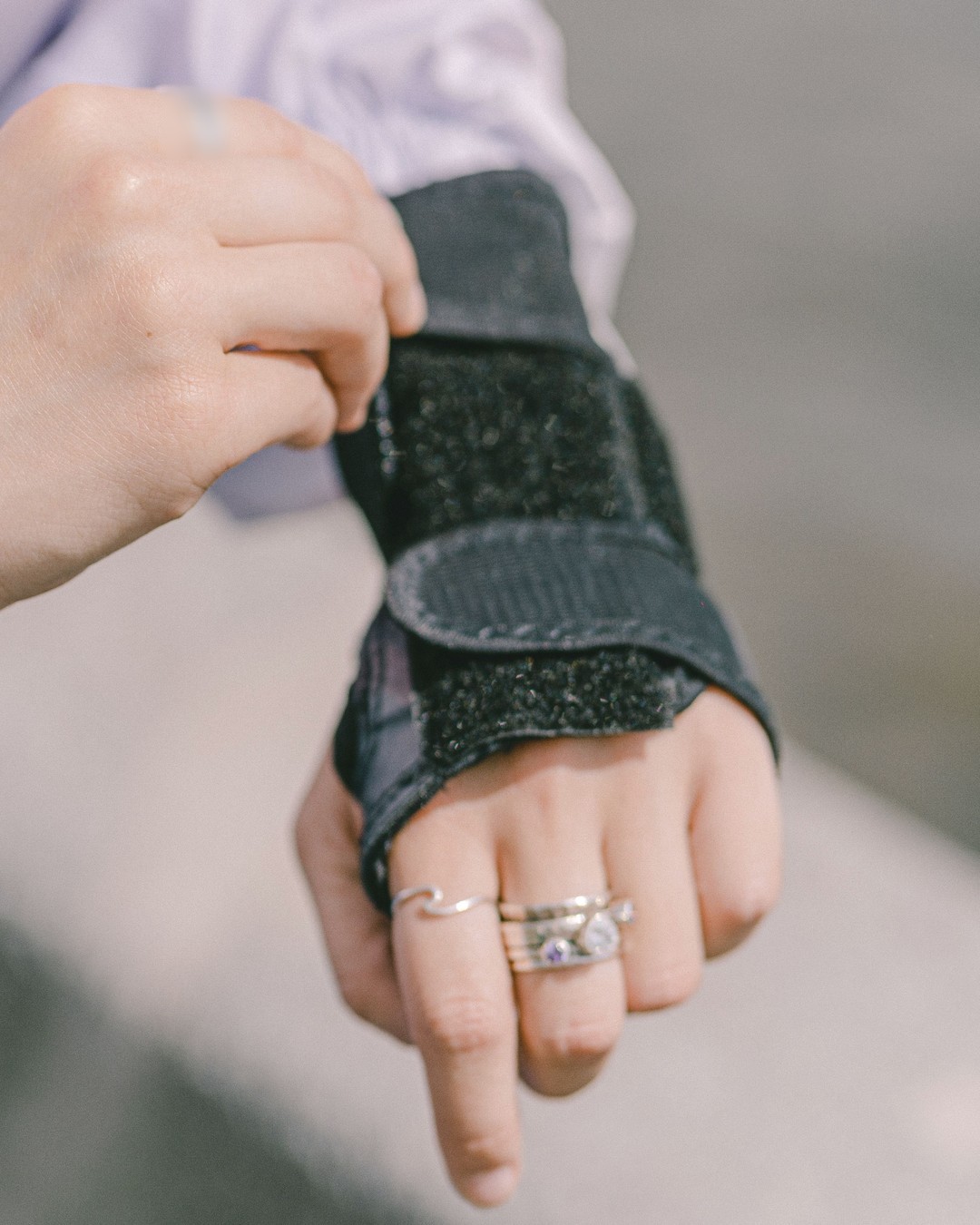 Close-up of one hand fastening the hook-and-loop straps of a plain black wrist splint on the other wrist outdoors, fingers left free