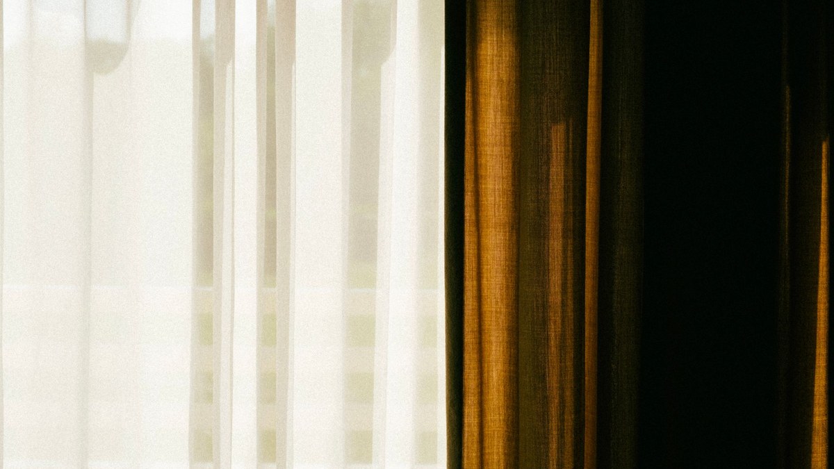 Daylight coming through a sheer white curtain beside a heavier drape in a quiet room