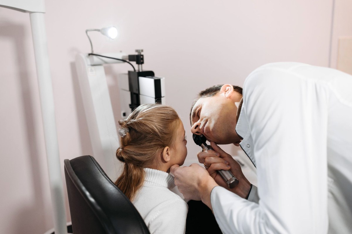 A clinician leaning in to look into a young girl's ear with an otoscope in a bright examination room