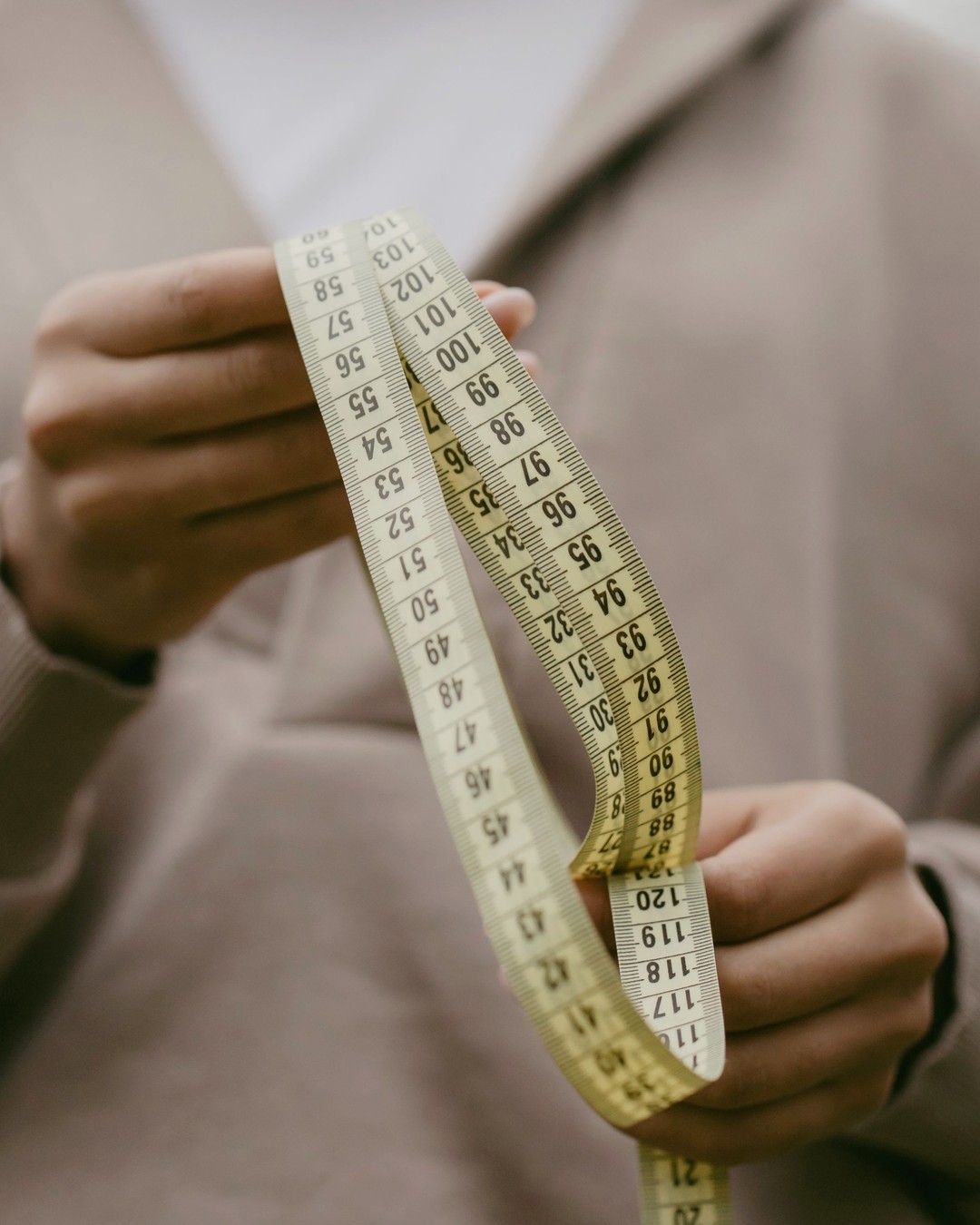 Two hands holding up a flexible tape measure in front of a beige sweater
