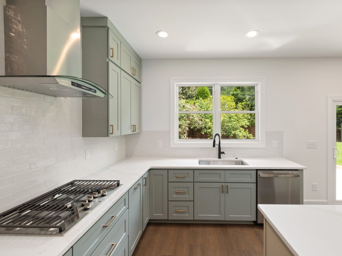 A bright kitchen with a glass canopy range hood mounted directly over a gas cooktop, daylight coming in through the window above the sink