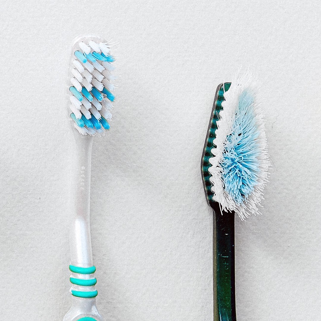 Two manual toothbrushes side by side on a white surface: one with bristles still straight, the other with its outer tufts splayed well past the edge of the head