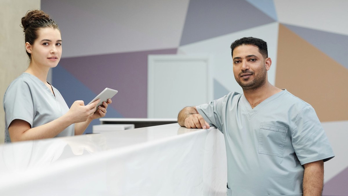 Two clinic staff in scrubs standing behind a bright reception desk
