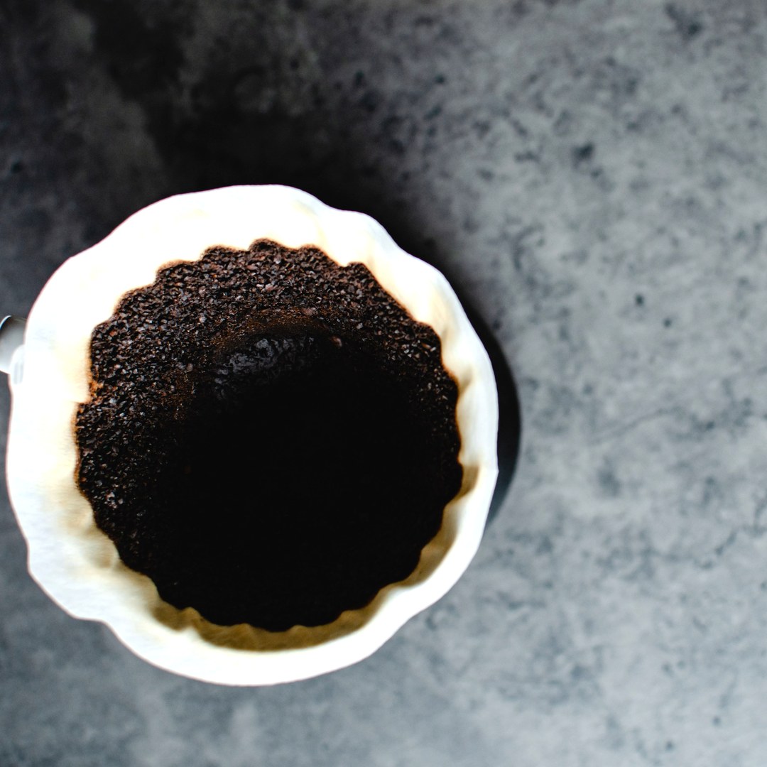 Used coffee grounds in a white paper filter seen from above on a grey counter