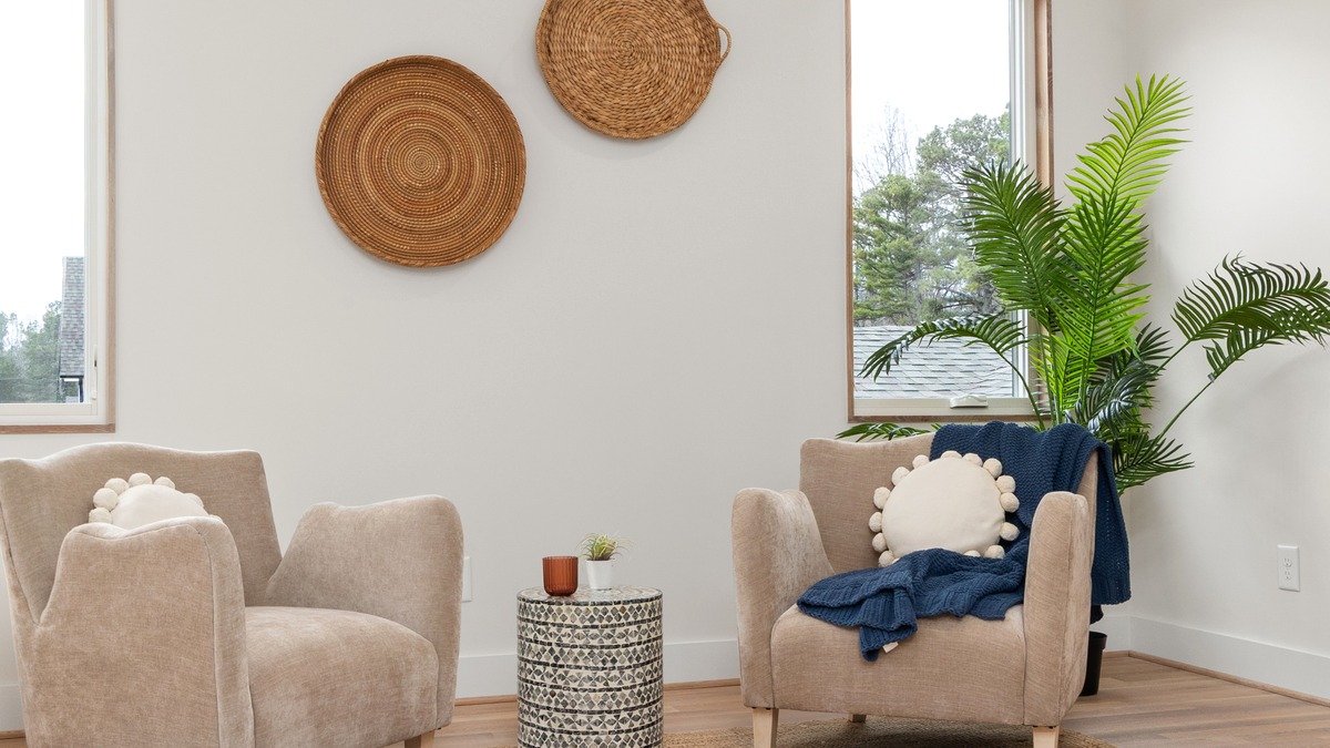 A bright, neutral-toned room with two upholstered armchairs facing each other across a small side table, a plant in the corner and daylight from two windows