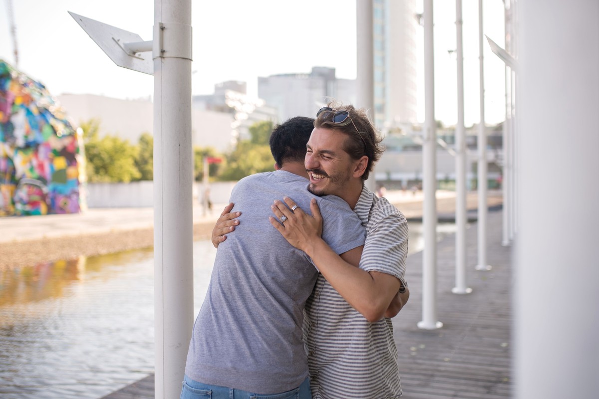 Two friends hugging in greeting on a sunlit waterfront boardwalk